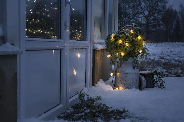 Sfeerbeeld van Konstsmide lichtsnoer bij een raam in de sneeuw, verlicht bij avondlicht