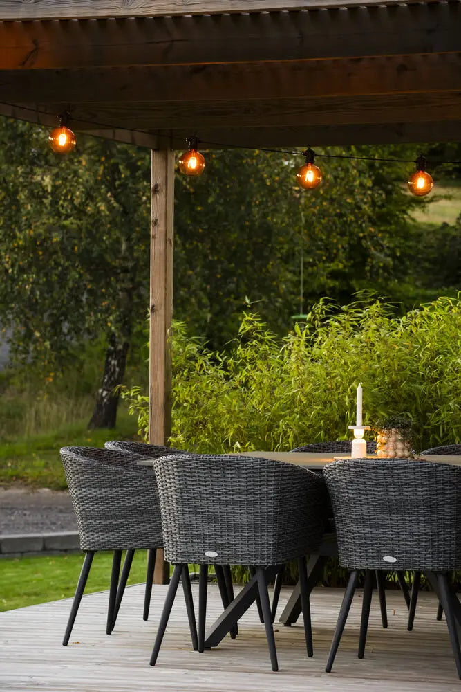 Konstsmide lichtsnoer opgehangen onder een overkapt terras, met eettafel en stoelen bij avondlicht