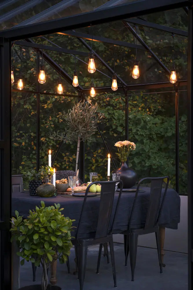 Konstsmide lichtsnoer opgehangen onder een overkapt terras met eettafel, verlicht bij avondlicht