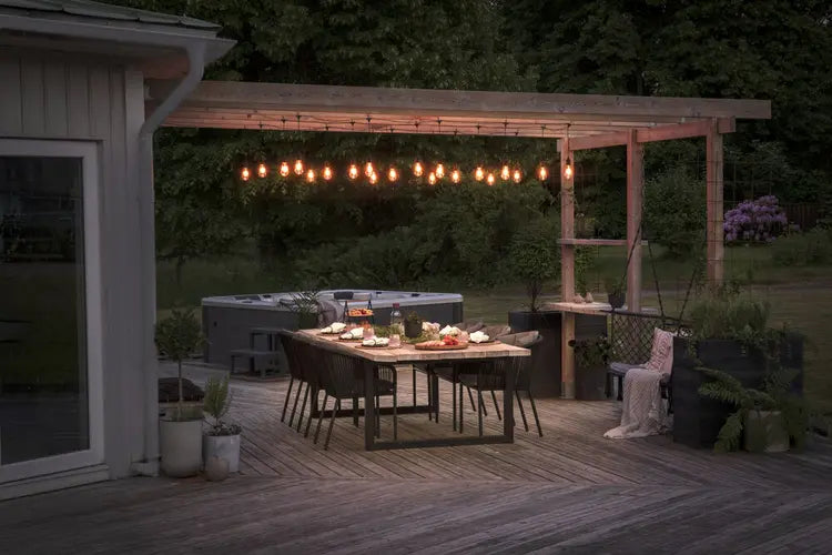 Konstsmide lichtsnoer opgehangen boven een terras naast een woning, verlicht bij avondlicht