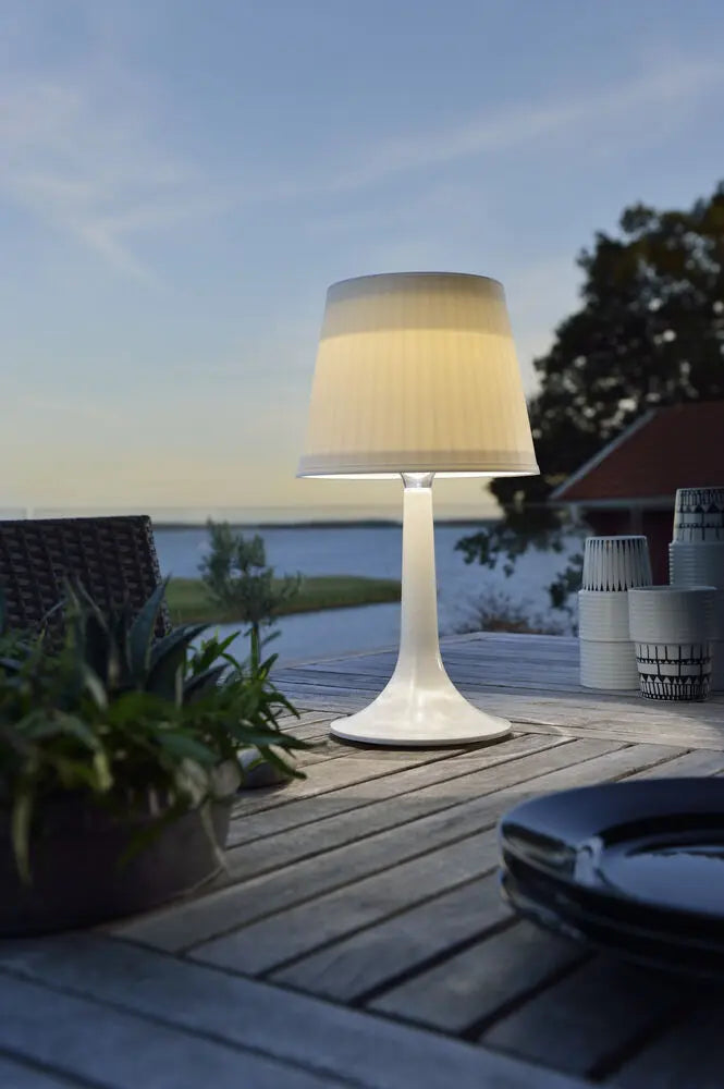 Konstsmide Assisi tafellamp op een terras bij zonsondergang, met uitzicht op het water