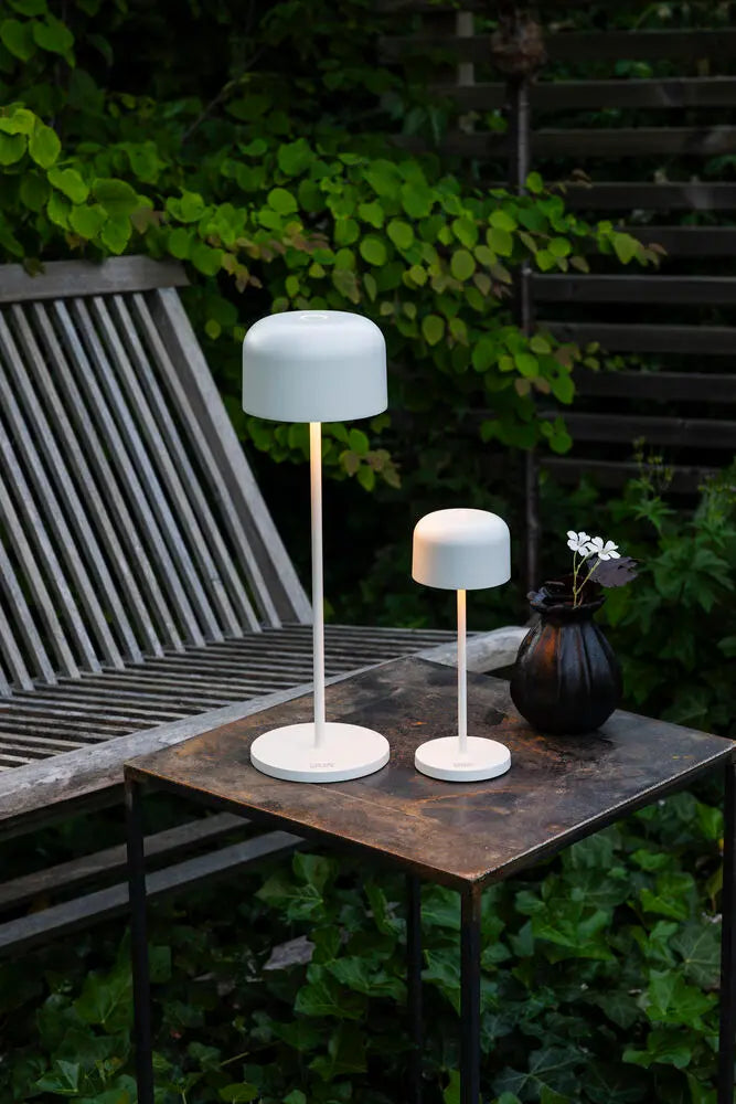 Konstsmide Lille tafellamp op een tuintafel met glazen, buiten bij groen