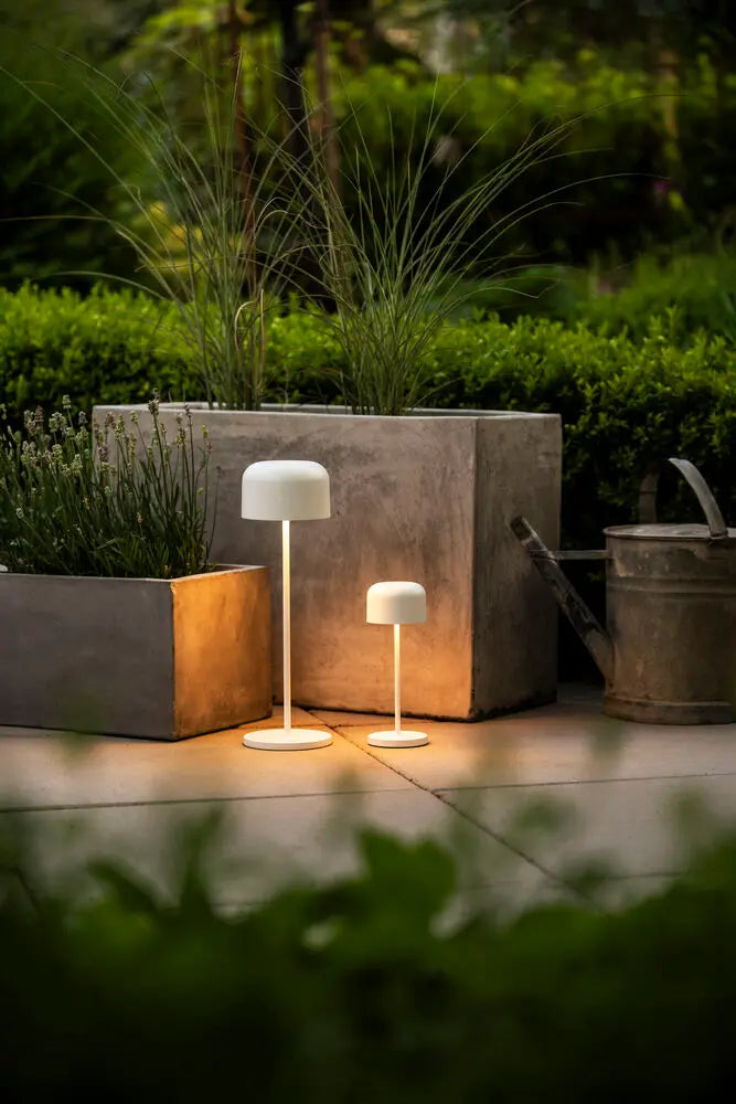 Meerdere Konstsmide Lille tafellampen op een terras bij een gemetselde muur, verlicht bij avondlicht