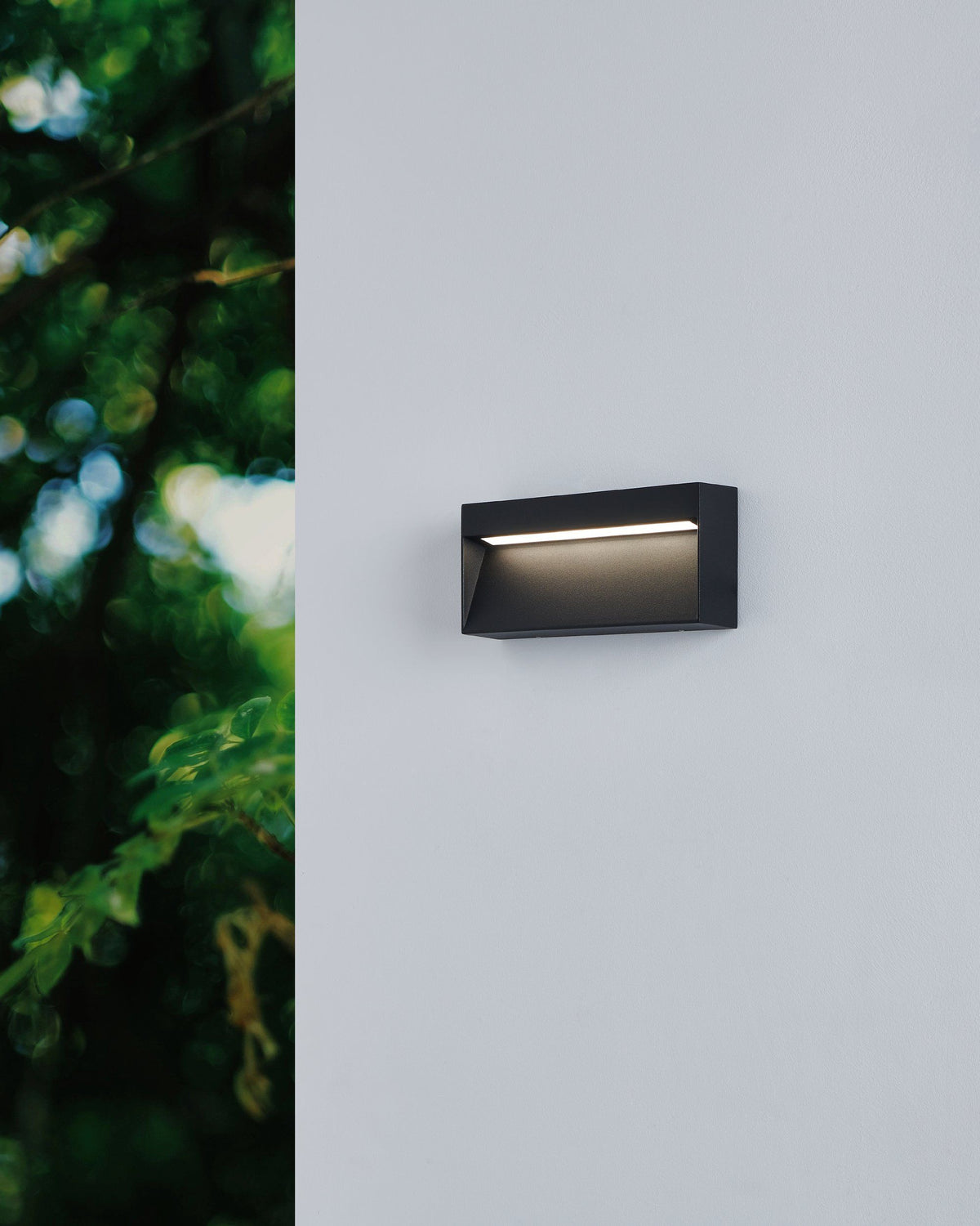 EGLO Marugio wandlamp gemonteerd aan een lichtgrijze gevel tussen groen