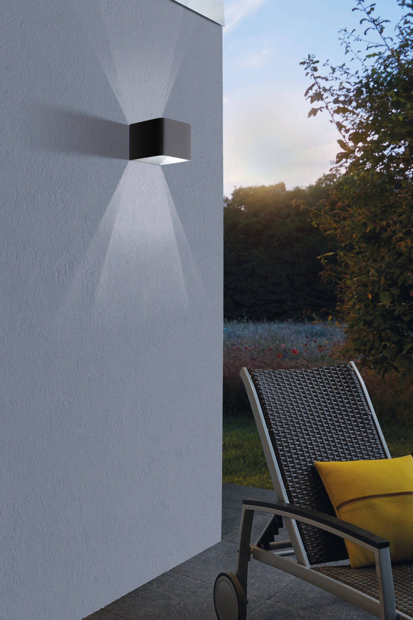 EGLO Doninni 1 wandlamp gemonteerd aan een gevel, verlicht bij avondlicht met terras op de achtergrond